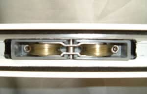 Close-up of a glass sliding door roller mechanism with two metal wheels mounted in a sleek grey frame.