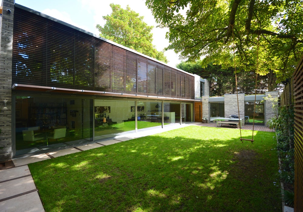 Modern garden extension with sliding doors opening onto manicured lawn, surrounded by mature trees and contemporary architecture.