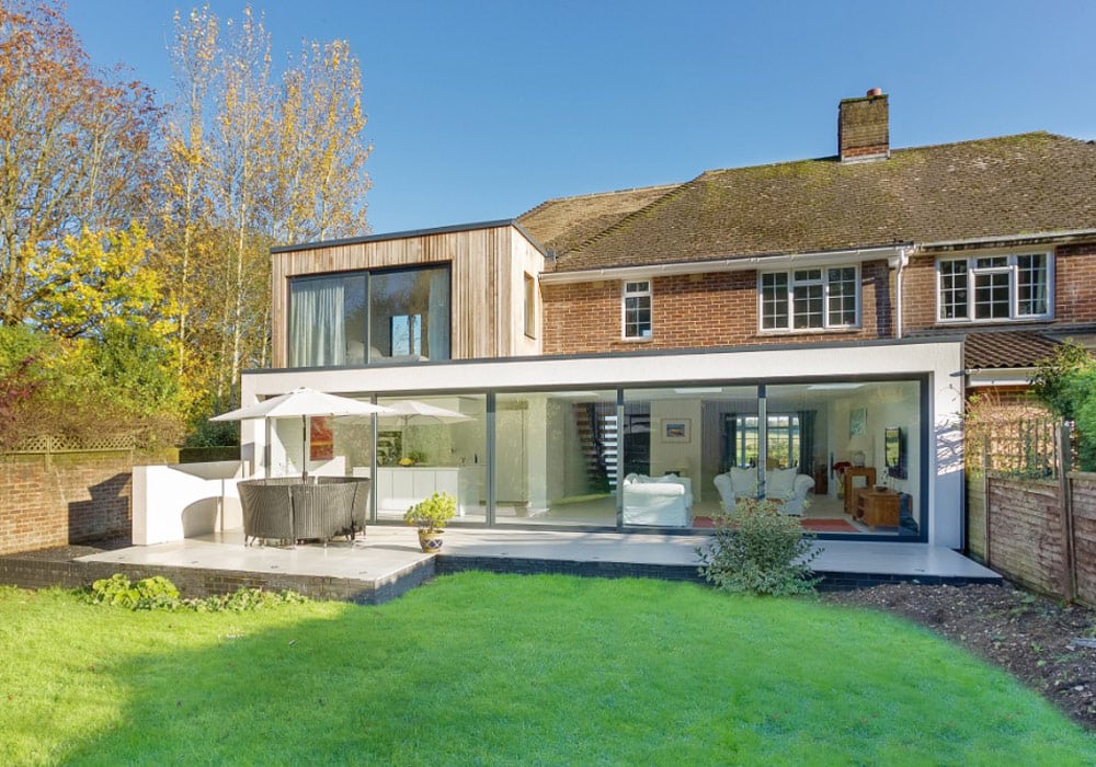 Modern home extension with expansive aluminium sliding doors and bifold doors opening onto a manicured garden beneath clear skies.