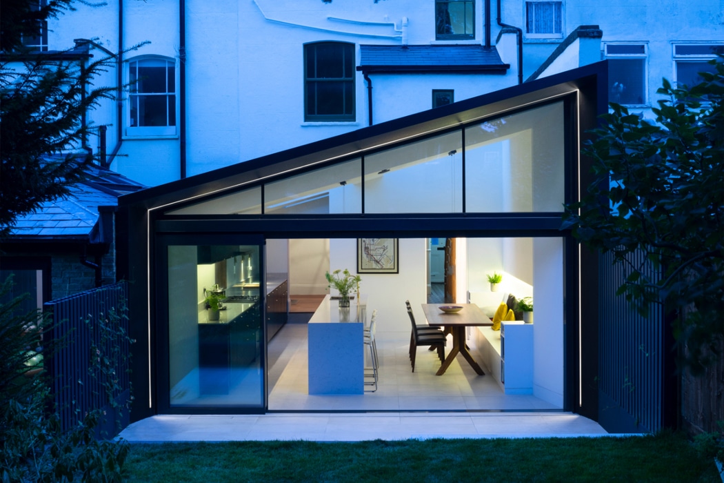 theEDGE2.0 ultra-slimline glass sliding door opening onto a modern kitchen-diner extension, showcasing minimalist framing and seamless indoor-outdoor living at dusk.