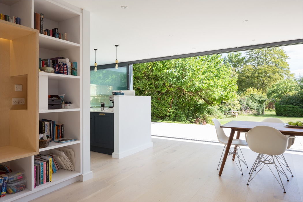 Modern open-plan kitchen and dining space with theEDGE2.0 ultra-slimline glass sliding doors opening onto a sunny garden with mature trees.