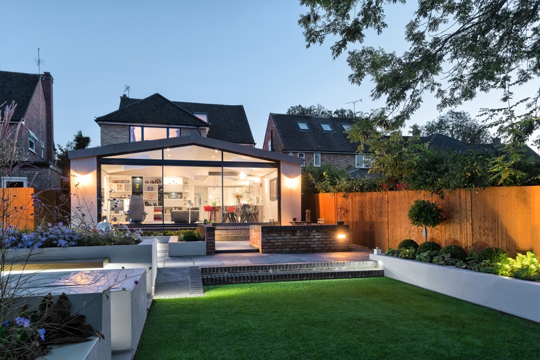 Modern garden extension with theEDGE2.0 glass sliding doors opening onto manicured lawn and seating area at dusk.