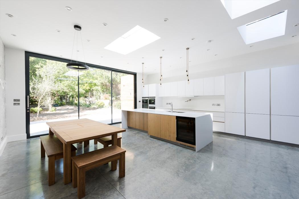 Modern kitchen with theEDGE2.0 ultra-slimline glass sliding doors opening onto a garden, featuring skylights and wooden dining table.