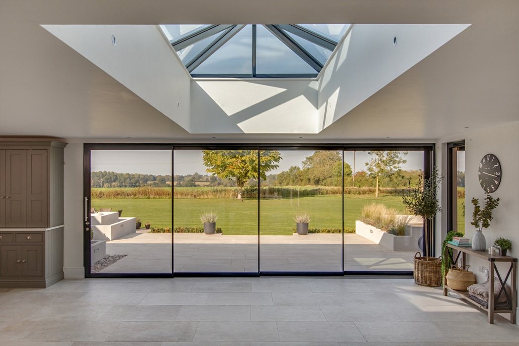 theEDGE2.0 ultra-slimline glass sliding door opening onto a sunlit patio overlooking expansive countryside views, with skylight above flooding the interior with natural light.